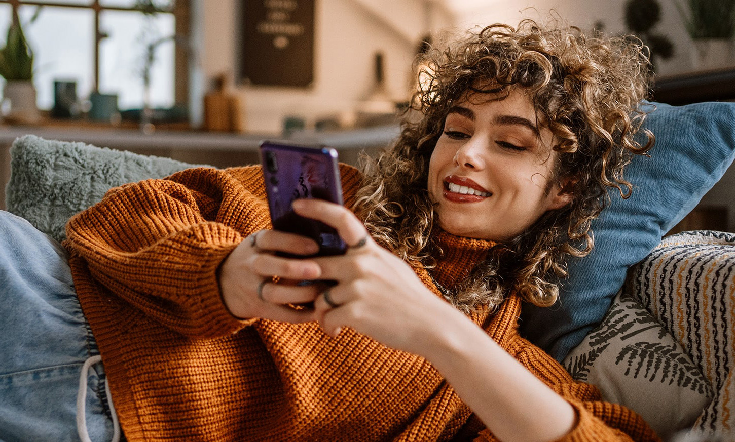 Jonge vrouw ligt op de bank met haar telefoon in handen