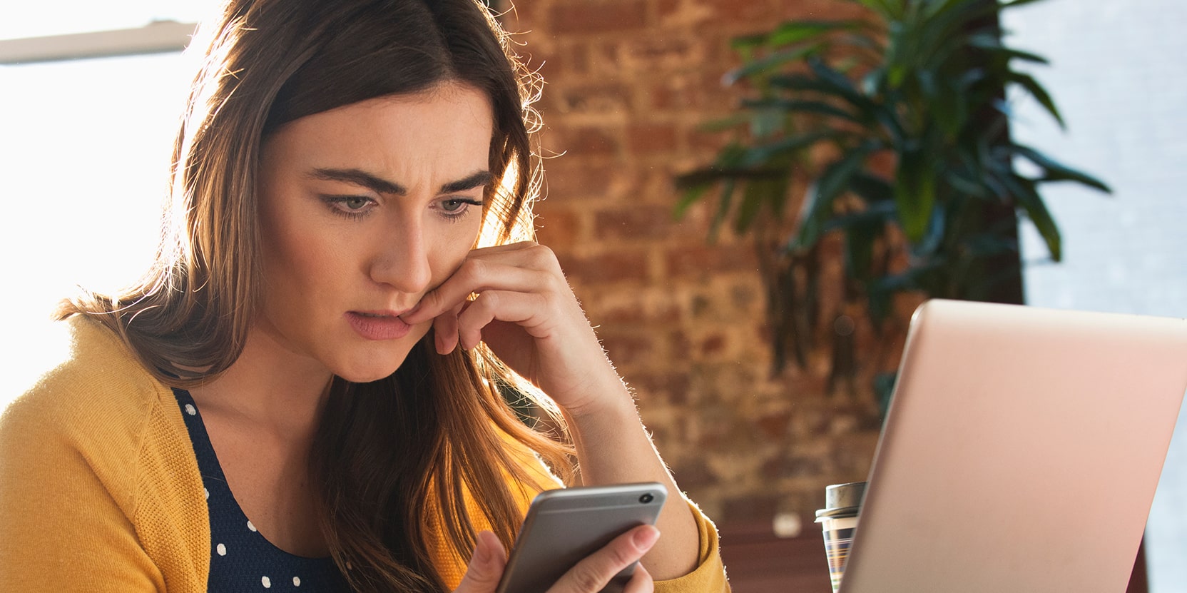 Iemand met laptop op tafel en telefoon in de hand